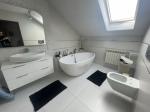 Łazienka wykafelkowana na biało z wanną, toaletą i umywalką z lustrem